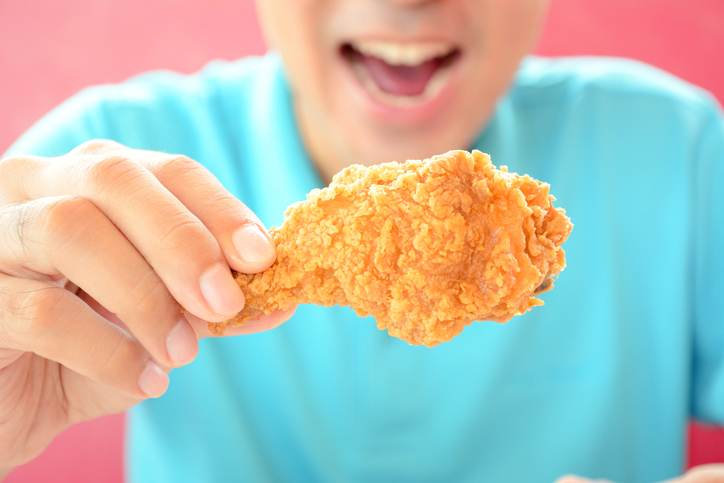 Young man holding  fried chicken leg, about to eat